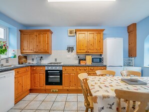 Una cocina con gabinetes de madera, estufa a gas, horno, microondas y una mesa con mantel de motivos caninos.