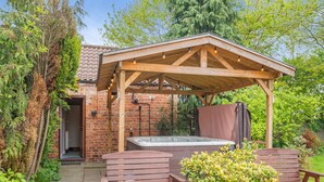 A wooden gazebo with a hot tub, two wooden benches, and a potted plant. - 3 bedroom accommodation in York (York)
