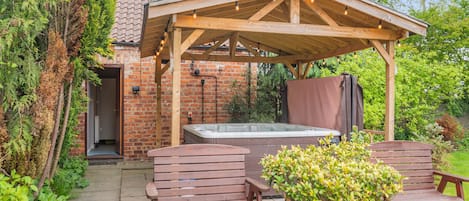 Eine Holzpergola mit Whirlpool, zwei Holzbanken und einem Topfpflanzen.