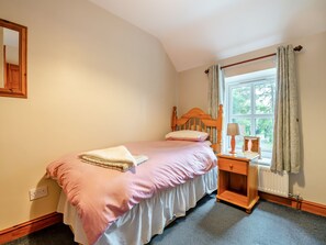 Un dormitorio con una cama individual, una mesita de noche, una ventana con cortinas y un radiador.