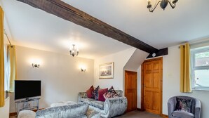 A living room with a sectional sofa, a grey armchair, a flat-screen TV, and wooden beams on the ceiling. - 3 bedroom accommodation in York (York)