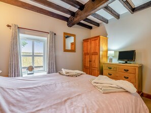 A bedroom with a bed, wooden wardrobe, and a television on a dresser.