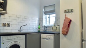 Een kleine keuken met een wasmachine, vaatwasser en een raam met gestreepte gordijnen.