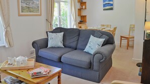 A cozy living room with a grey sofa, a wooden coffee table, and a dining area in the background.