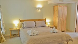 A neatly made bed with pillows, two bedside lamps, and a wooden wardrobe in a room with beige walls and carpet.