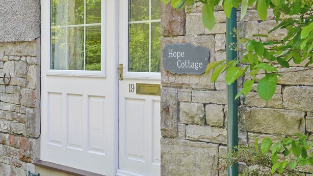 A cottage with a white door, a stone wall, and a sign that reads "Hope Cottage."