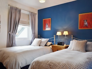 Ein Zimmer mit zwei Betten, einem Vorhangfenster, zwei Nachttischlampen und zwei gerahmten Bildern an der Wand.