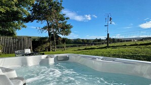 Un bain à remous dans un jardin, avec une clôture en bois, des arbres et un ciel dégagé.