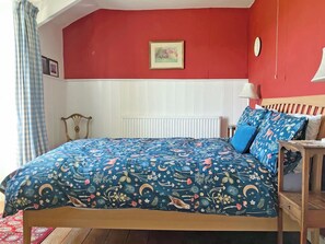 Une chambre à coucher avec un lit, une table de chevet, une lampe, une fenêtre avec des rideaux et une horloge murale.