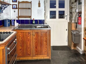 A kitchen with wooden cabinets, a stove, a sink, and a stone wall. - 2 bedroom accommodation in Trebarwith, near Delabole (Trebarwith, near Delabole)