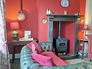 Une pièce avec un mur rouge, un canapé en cuir, une petite table avec une lampe et un poêle à bois.