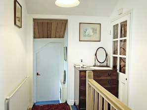 A hallway with a wooden door, a mirror, a small table with toiletries, and a framed picture on the wall.