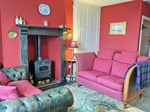 Un salon avec un mur rouge, un poêle à bois noir, un canapé rose et un fauteuil en cuir vert.