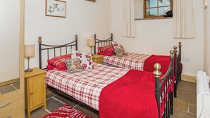 Slaapkamer met twee bedden, een houten nachtkastje, een rood kleed, een lijst met een afbeelding aan de muur, en een raam met gordijnen.