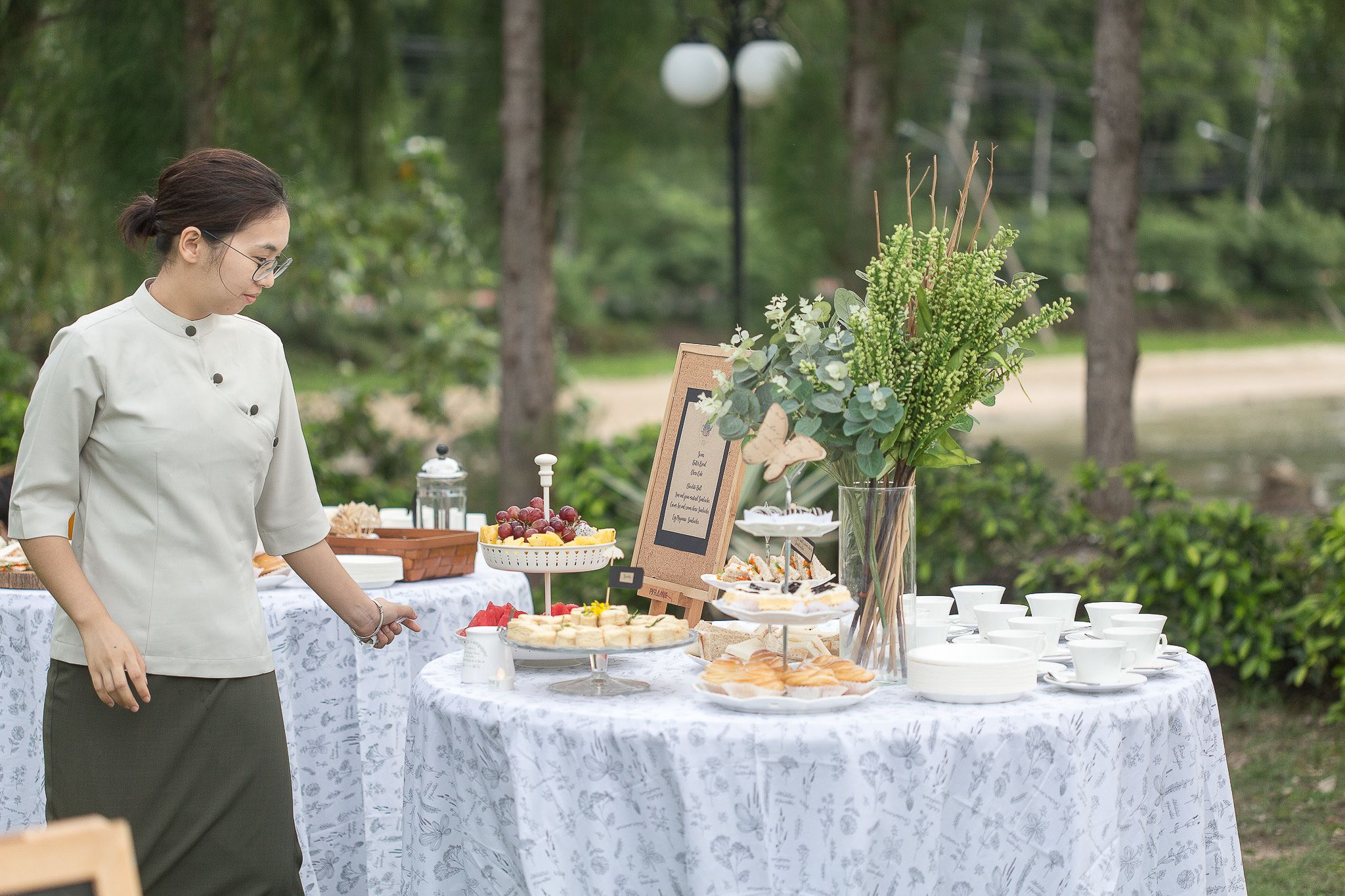 Une table dressée avec divers plats et un panneau indicateur, le tout entouré de verdure.