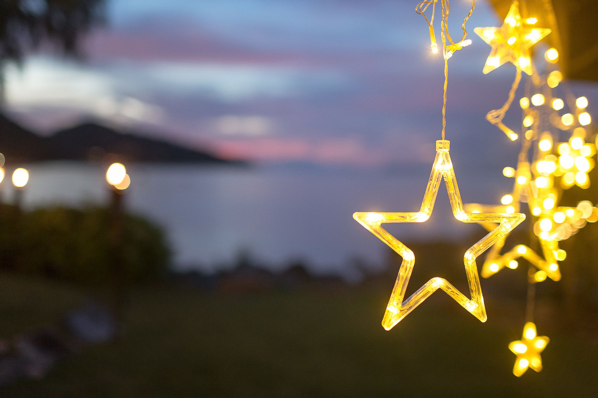 A star-shaped light decoration hanging outdoors with a blurred background of a body of water and mountains.