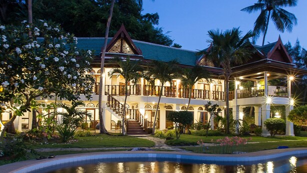 Un gran complejo turístico de varios pisos con piscina, palmeras y una fachada iluminada al atardecer.