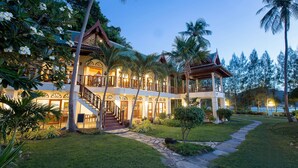 Un resort de dos pisos con una escalera central, rodeado de exuberante vegetación y palmeras.