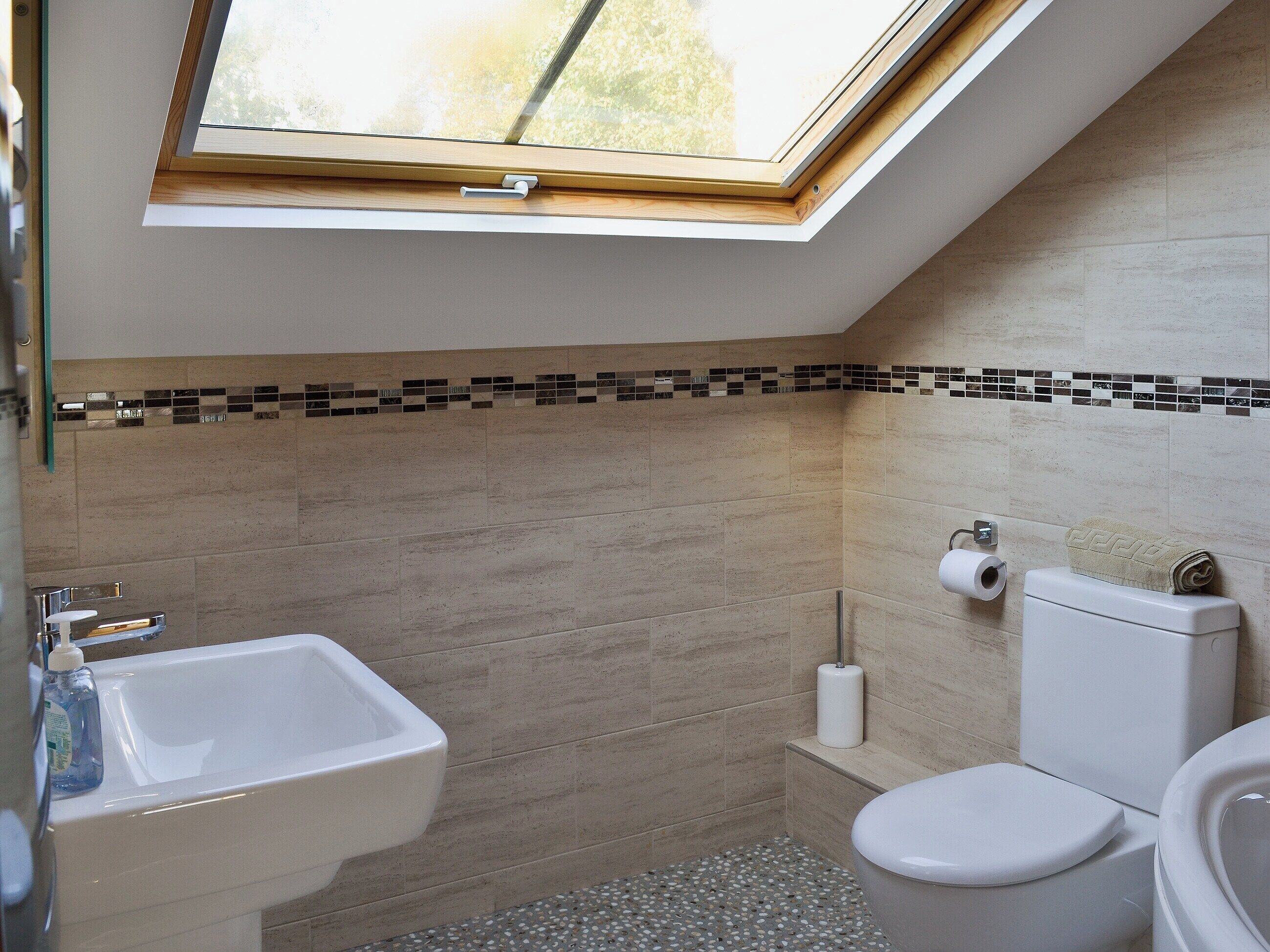 A modern bathroom with a skylight, a sink, toilet, and a small shelf with toiletries.