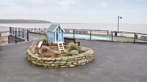 A small blue and white beach hut with a ladder, surrounded by a stone wall and a bench.