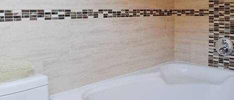 A bathroom with a white bathtub, a toilet, and a tiled wall with a mosaic border.