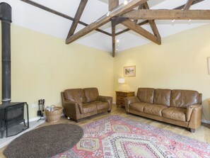 A cozy living room with two leather sofas, a patterned rug, a fireplace, and a wooden ceiling structure.