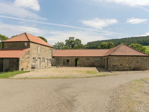 A stone building with a red-tiled roof, a gravel driveway, and a grassy area.