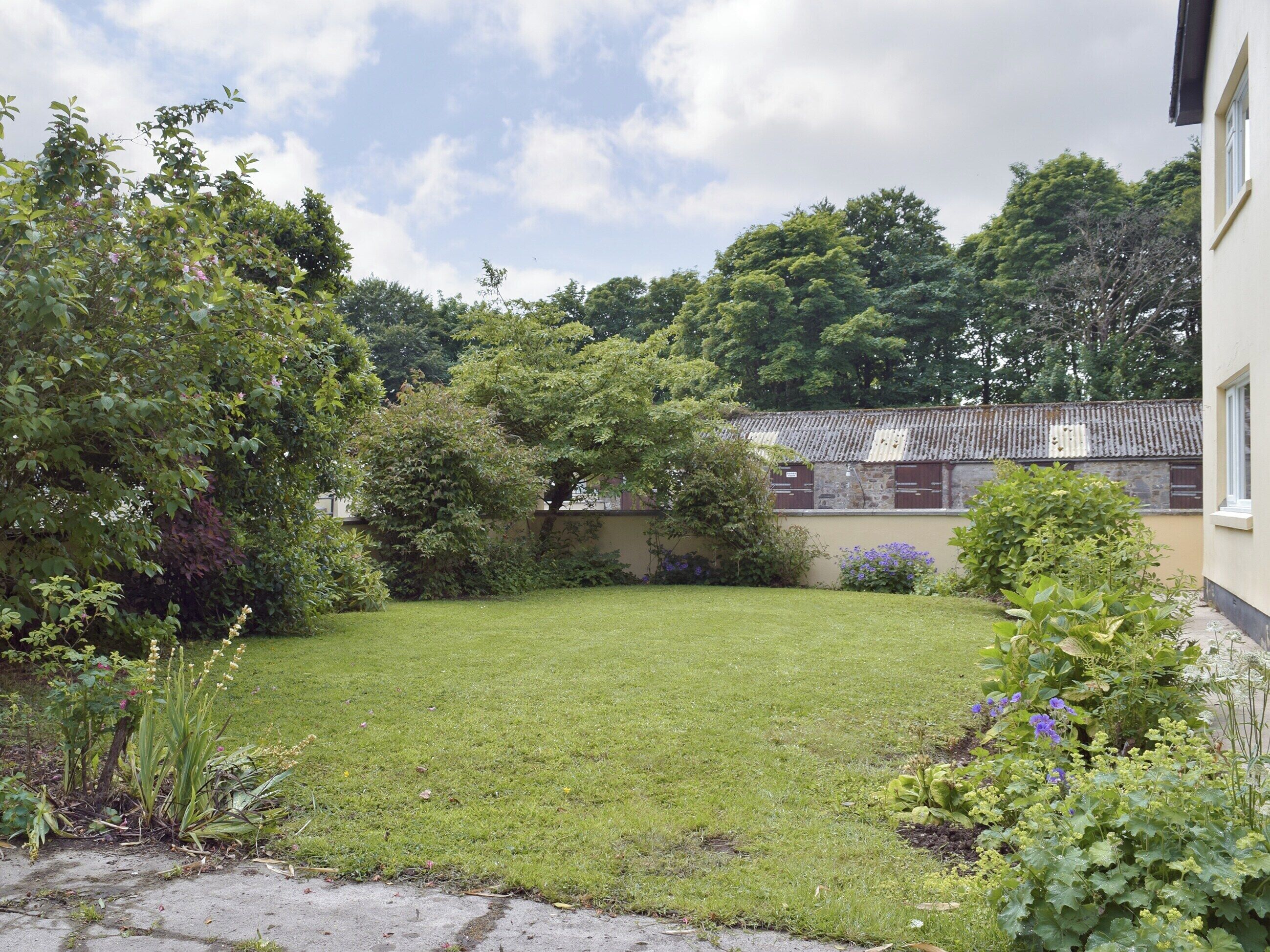 A well-maintained grassy yard with a stone wall, surrounded by various shrubs and trees.