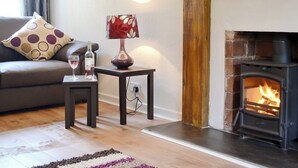 Un salón acogedor con chimenea, un sofá con cojines estampados, una mesita con una botella de vino y una lámpara.