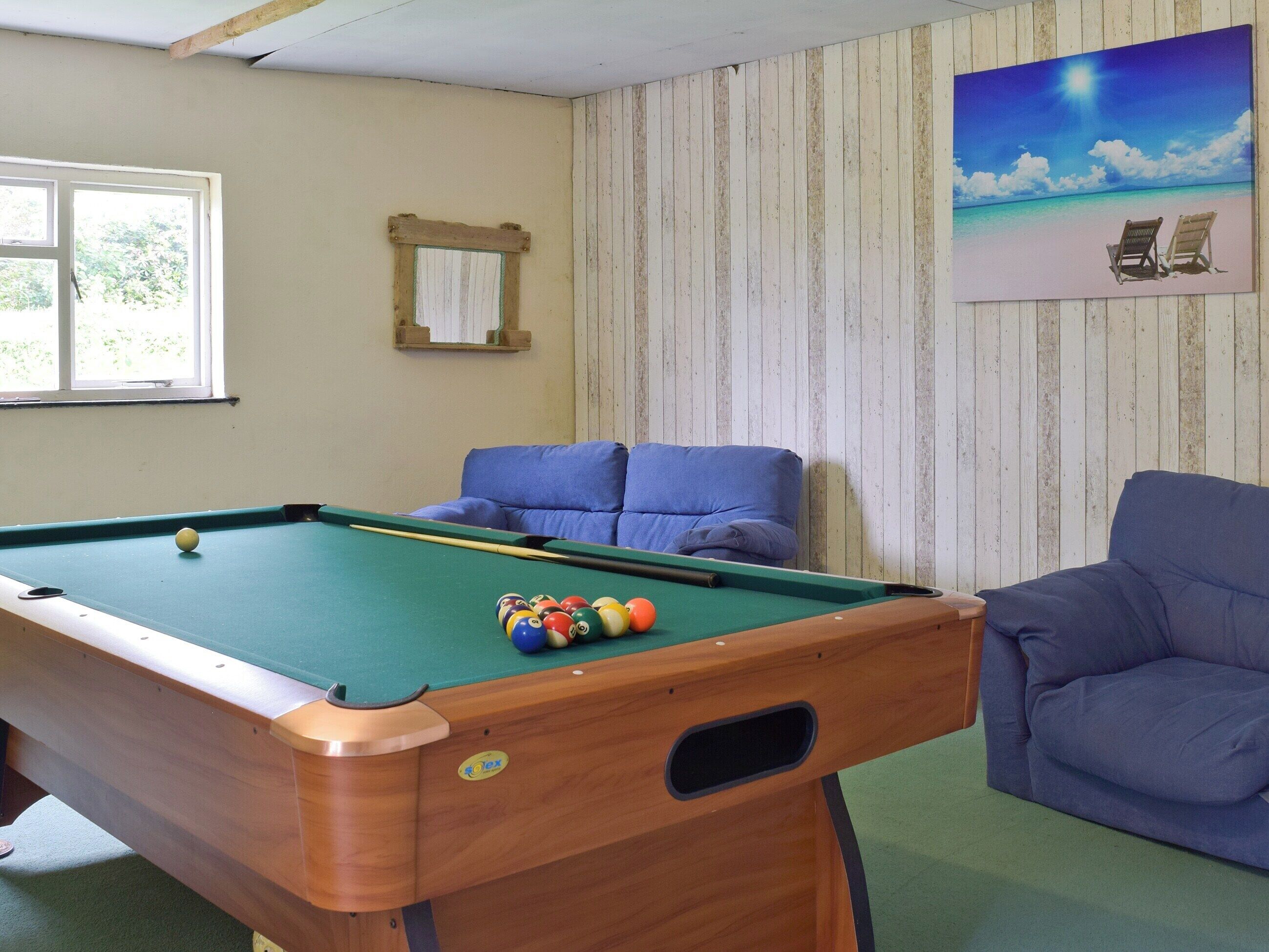 Une table de billard avec des billes, un canapé bleu et un tableau représentant une scène de plage.