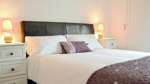 Una cama bien hecha con ropa de cama blanca y marrón, dos mesitas de noche con lámparas y un armario blanco.