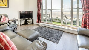 Un salon comprenant un canapé, une table basse, un téléviseur et une grande fenêtre donnant sur la plage.