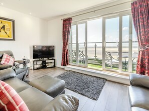 A living room with a sofa, a coffee table, a TV, and a large window with a view of the beach.