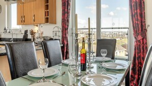 Un coin repas avec une table dressée pour quatre personnes, une bouteille de vin et une vue sur la ville grâce à de grandes fenêtres.