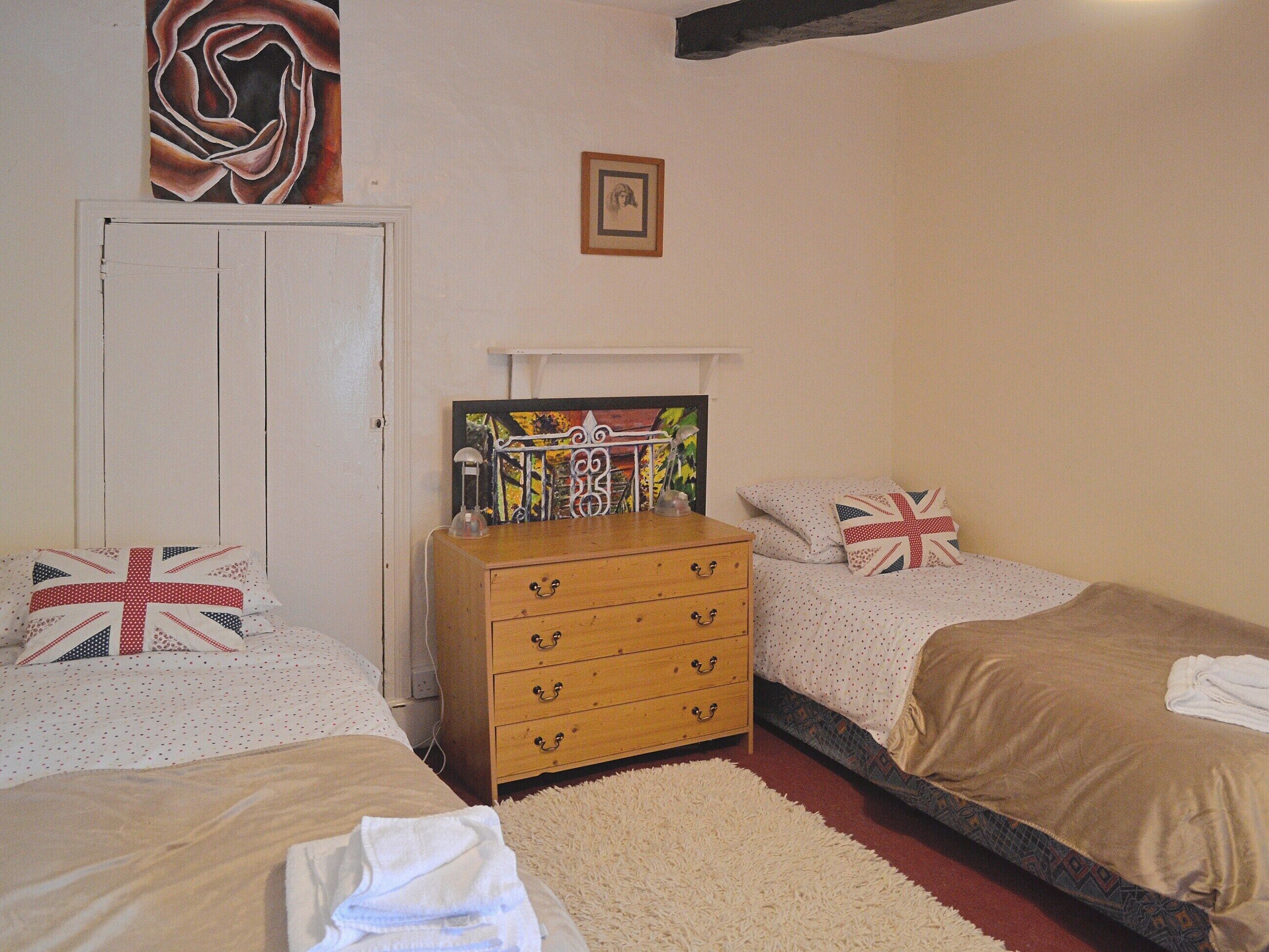 A bedroom with two single beds, a wooden dresser, and a white door.