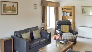 A living room with a leather sofa, a wooden coffee table, a black leather armchair, a bookshelf, and a radiator. - 1 bedroom accommodation in Lowick Bridge (Lowick Bridge)