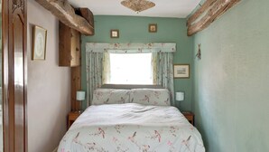 A bedroom with a floral bedspread, a window with floral curtains, and a wooden ceiling beam. - 1 bedroom accommodation in Lowick Bridge (Lowick Bridge)