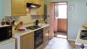 A kitchen with wooden cabinets, a stove, an oven, and a microwave. There is a window and a door leading to another room. - 1 bedroom accommodation in Lowick Bridge (Lowick Bridge)
