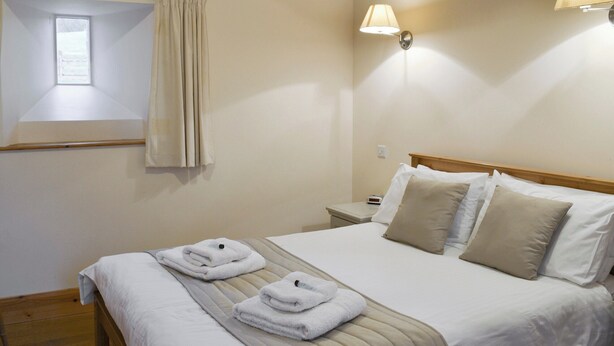 Een hotelkamer met een bed, twee nachtkastjes, een raam met gordijnen en een wandlamp.
