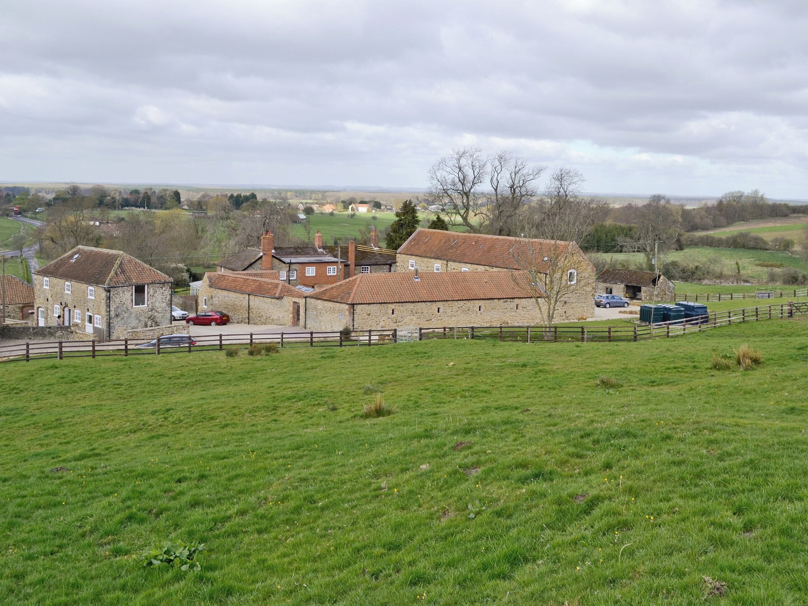 A stone building with multiple rooms, surrounded by a fenced area and a grassy field.