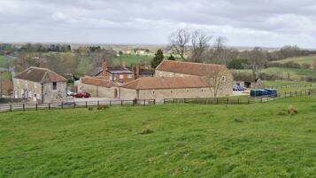 A stone building with multiple rooms, surrounded by a fenced area and a grassy field.