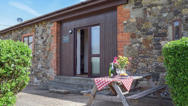 A stone cottage with a wooden door, a sign reading "Apple Tree Cottage," and a table with a checkered tablecloth outside. - 3 bedroom accommodation in Brighstone (Brighstone)