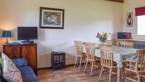 A cozy living room with a sofa, a TV, a small table with chairs, a wooden cabinet, and a framed picture on the wall. - 3 bedroom accommodation in Brighstone (Brighstone)