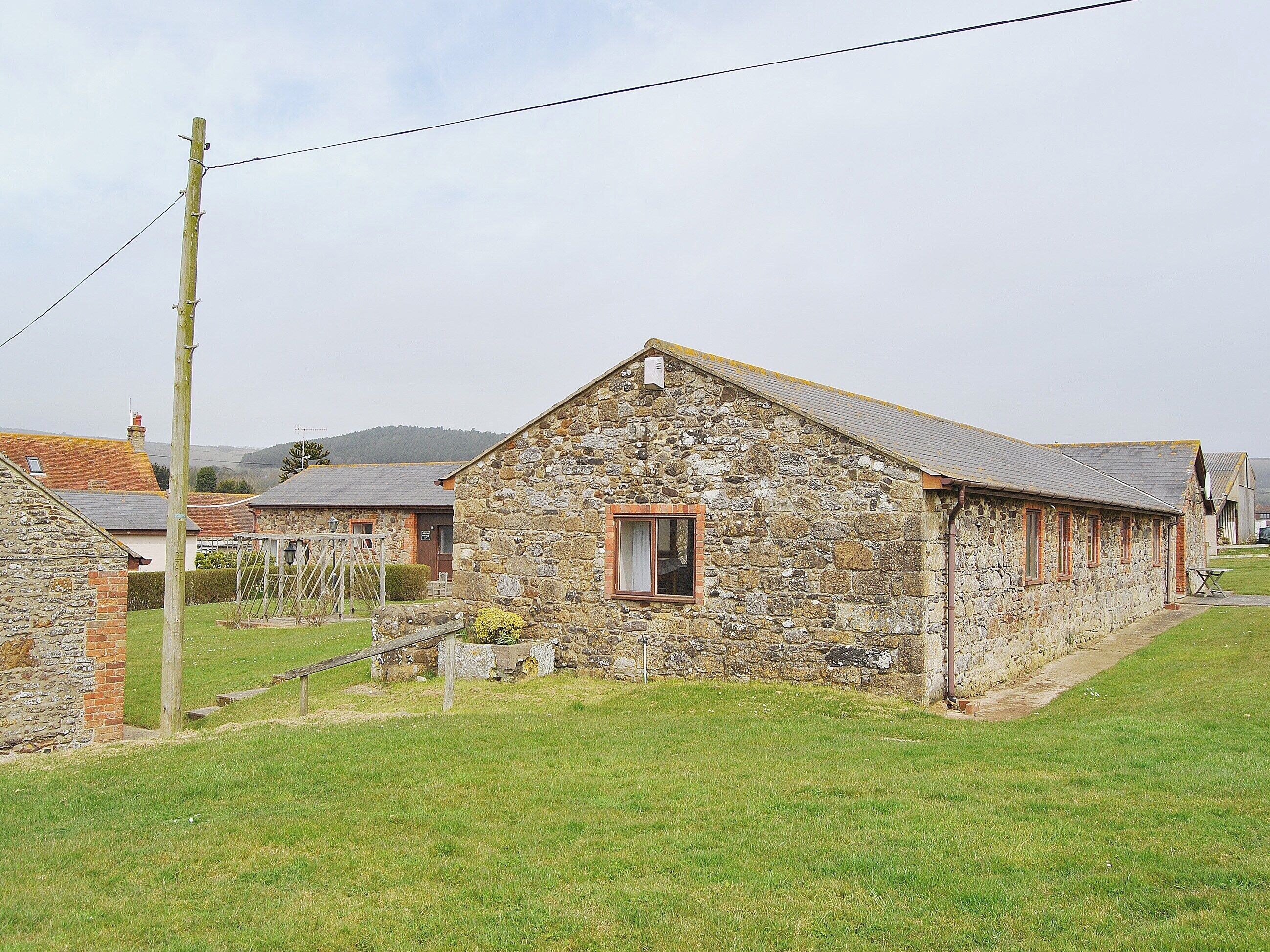Un edificio de piedra con un ventanal pequeño, rodeado de un área con césped y otros edificios de piedra.