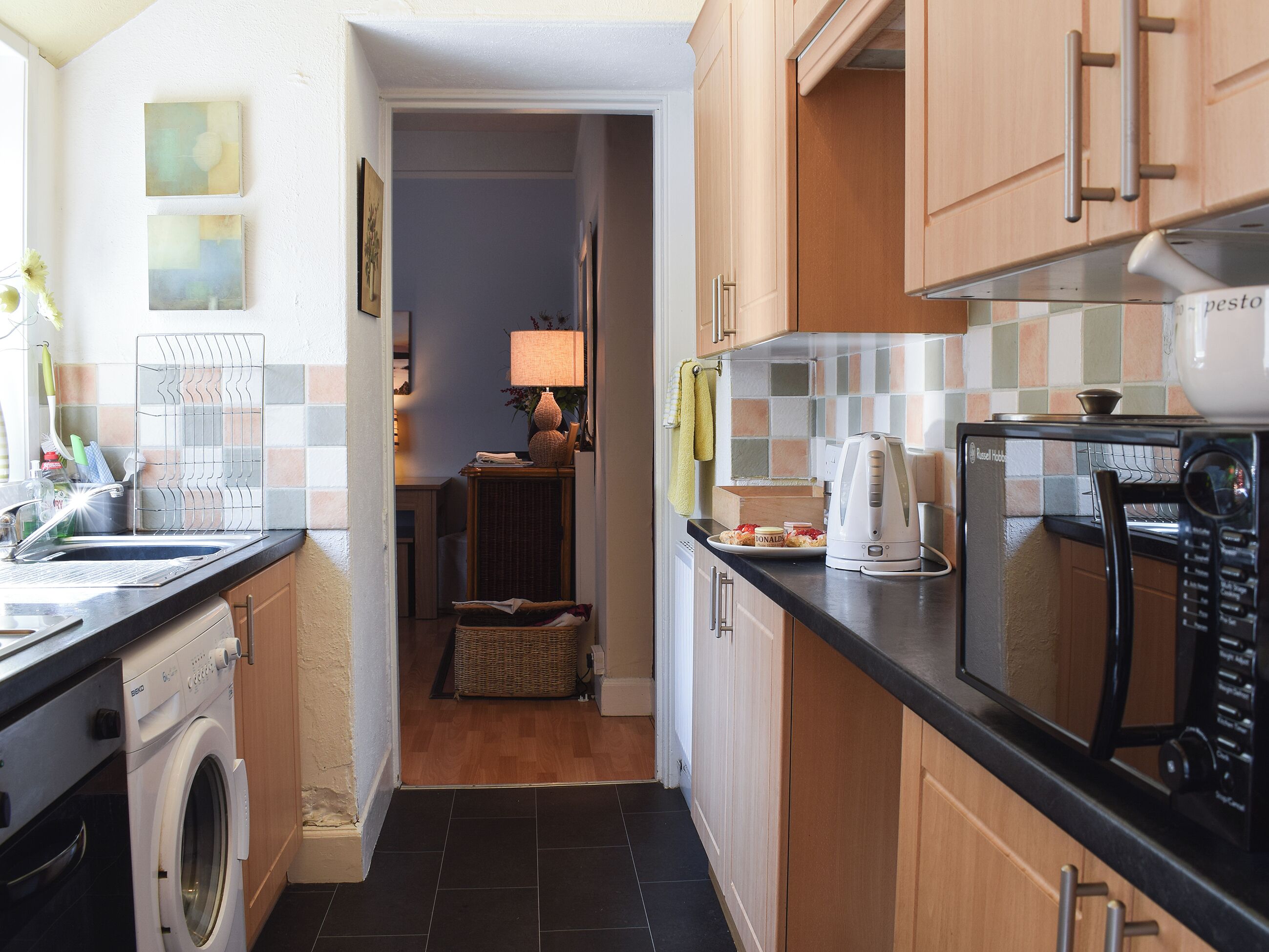 A compact kitchen with a washing machine, a microwave, and a dining area visible in the background.