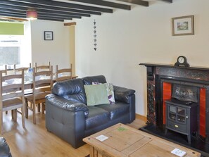 A living room with a leather sofa, wooden chairs, a fireplace, and a dining table. - 3 bedroom accommodation in Nefyn, near Pwllheli (Nefyn, near Pwllheli)