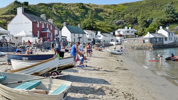 Un pueblo junto a la playa con una hilera de edificios blancos, incluyendo una señal visible que dice 'TY COCH INN'.