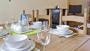 Una mesa de comedor dispuesta con vajilla blanca, vasos, una jarra azul y una silla de madera.