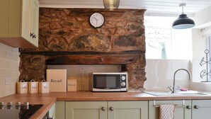 Una cocina con pared de piedra, un reloj, microondas y recipientes de almacenamiento etiquetados.