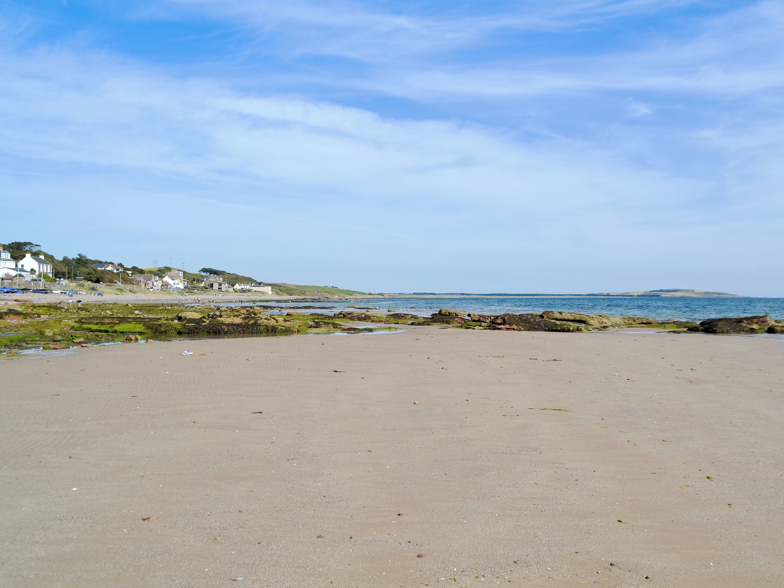 A beach with a rocky shoreline, a clear sky, and houses in the background.